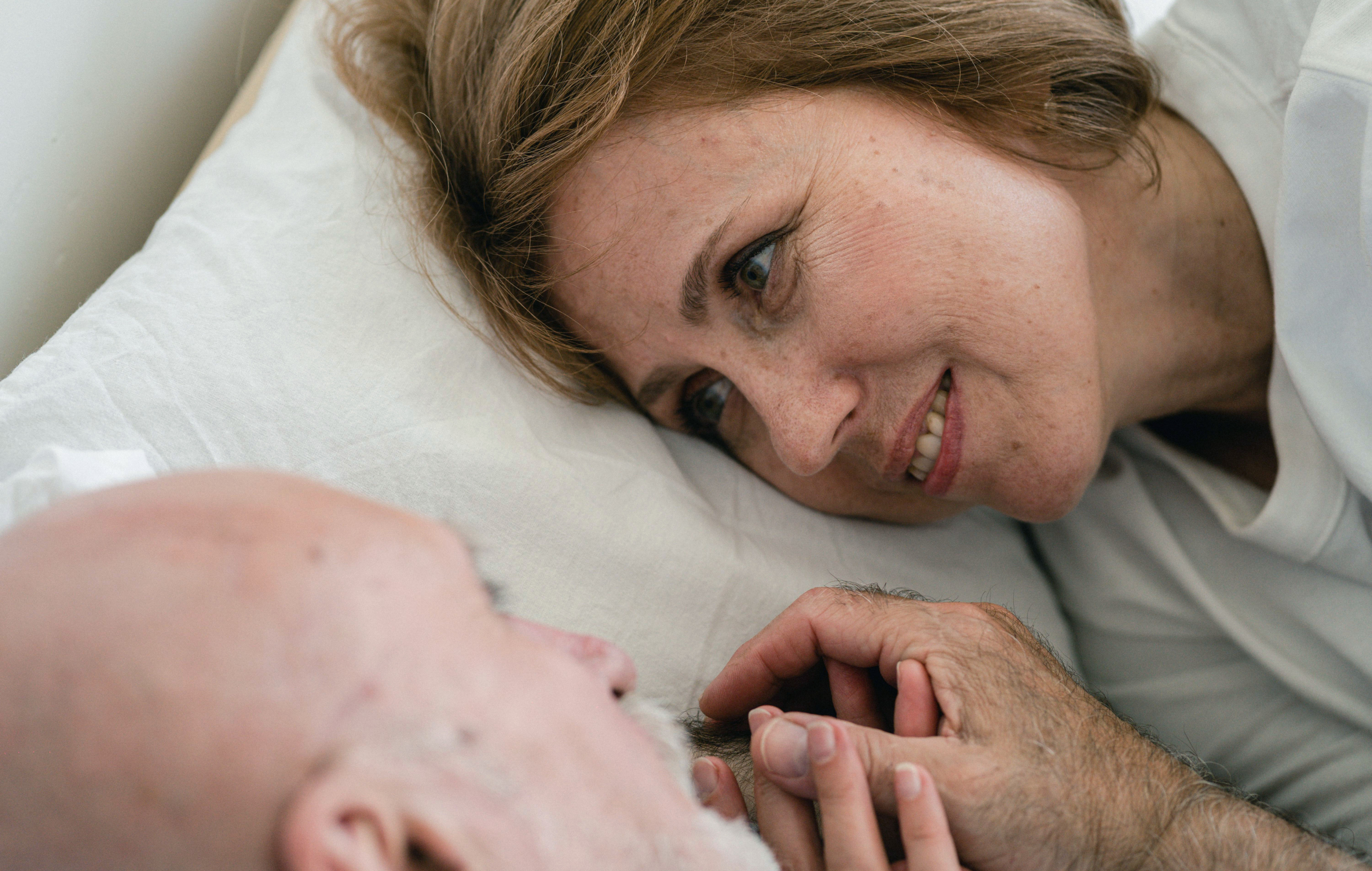 Een man en vrouw liggen samen in bed en kijken elkaar liefdevol aan